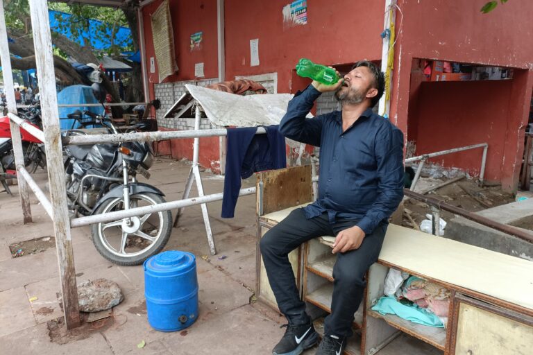 Mohammad Nasim takes a sip of water from an old bottle next to his shoe cart. The 40-year-old street vendor recalls how a fellow vendor was hospitalised this summer due to severe heat illness. He says they work on the street for 14 hours a day, suffering heat, humidity and vehicle fumes. Image by Anuja.