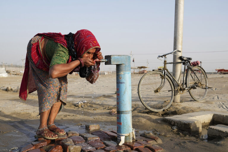 A woman stops to drink water from a public tap on a hot summer day in Prayagraj in 2024. (AP Photo/Rajesh Kumar Singh)