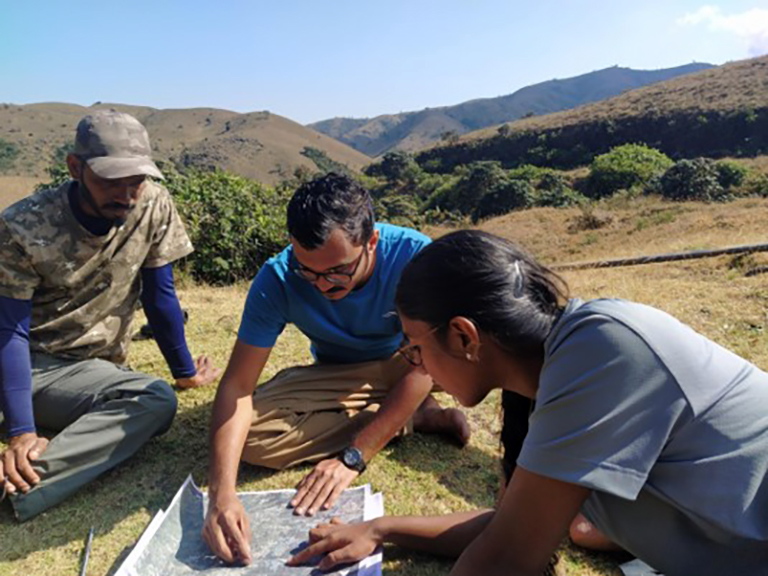 (L-R) Chandrasekar Das, Akshay Anand and Amrutha Rajan read a map in the Nilgiris' montane shola grasslands. Image by Vijay Ramesh.