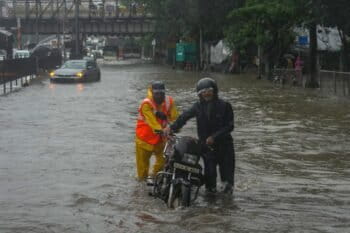 A municipal worker helps a man push his bike through a waterlogged road following heavy rains in Mumbai. (AP Photo/Rafiq Maqbool)