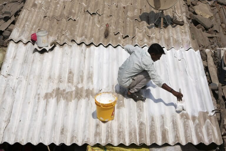 A man applies reflective paint to the roof of a house to cool the indoors in Ahmedabad. (AP Photo/Ajit Solanki)