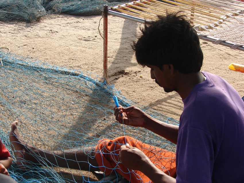 A fisher repairs a net on a beach in Gujarat. Traditional livelihoods like fishing and farming are threatened by salinity in fields and chemical pollution in the sea. Image by Ravleen Kaur.
