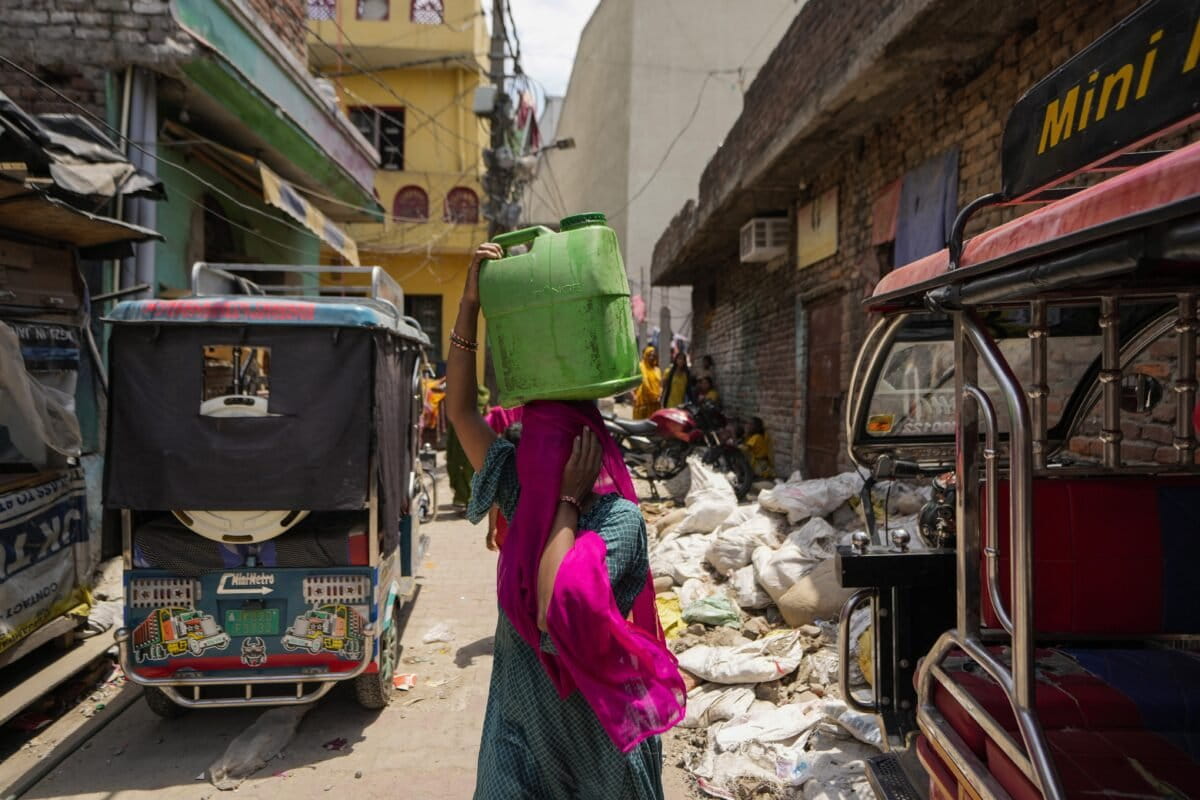 A woman carries water collected from a public tap during the summer on the outskirts of Jammu. (AP Photo/Channi Anand, File)