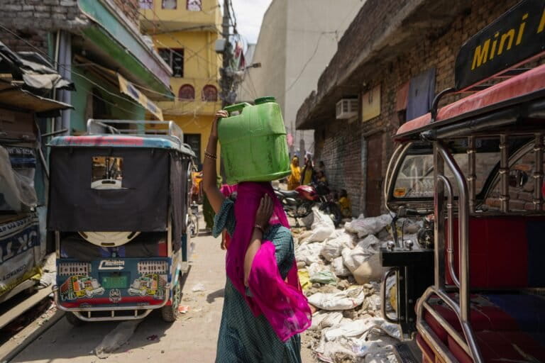 A woman carries water collected from a public tap during the summer on the outskirts of Jammu. (AP Photo/Channi Anand, File)