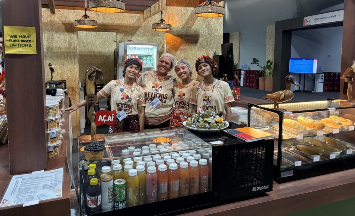 एना क्लारा ब्रांडाओ, उनकी सहकर्मी एमिली और टीम के बाकी सदस्य बेलेम के कॉप30 ब्लू ज़ोन में एक परिवार द्वारा संचालित स्टॉल "डेलिसियास क्विलोम्बोलास" में पारंपरिक अमेज़नियन भोजन परोसते हुए। छोटे उत्पादक और समुदाय-संचालित रसोई सम्मेलन में भोजन उपलब्ध करा रहे हैं। तस्वीर - मनीष चंद्र मिश्रा